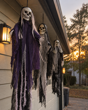 Close-up of three Skeleton Trio figures hanging along a porch at sunset